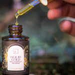 clean beauty brand jamaRoots Liquid Gold natural face serums dropper of frankincense and calendula oil as hand holds dropper over glass bottle